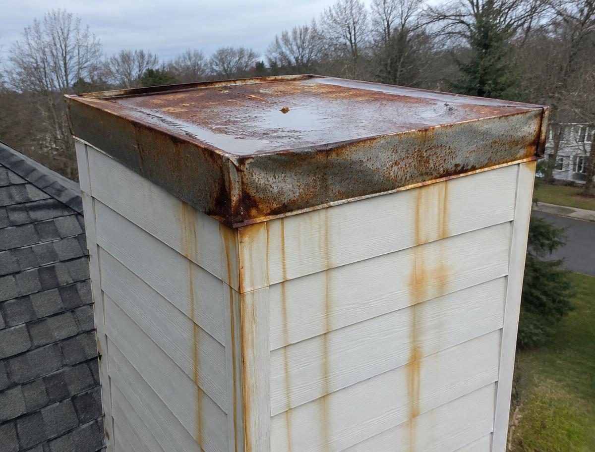 Rusted chimney chase cover with a damaged rain cap on a Texas home