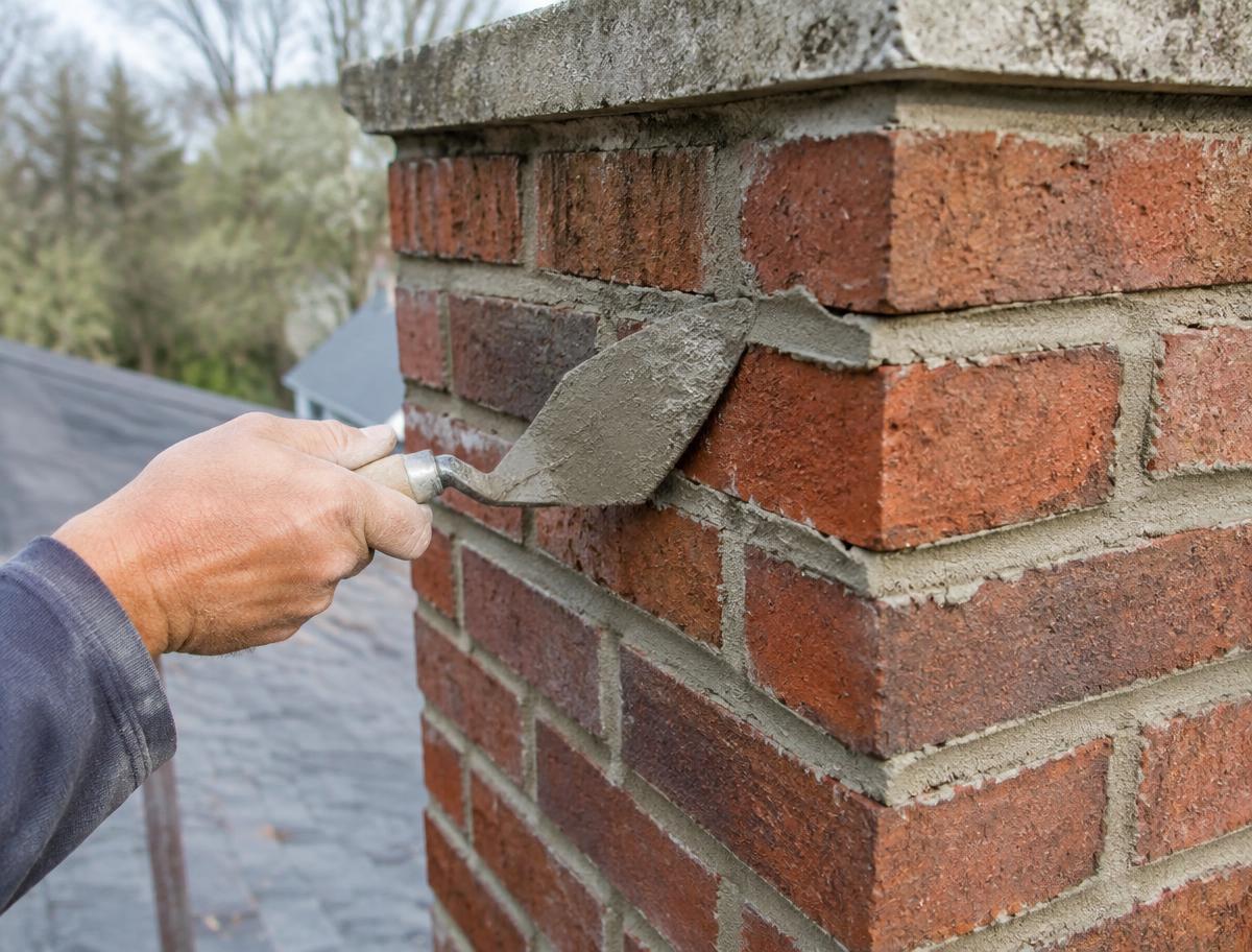 Technician repointing mortar joints on a brick chimney